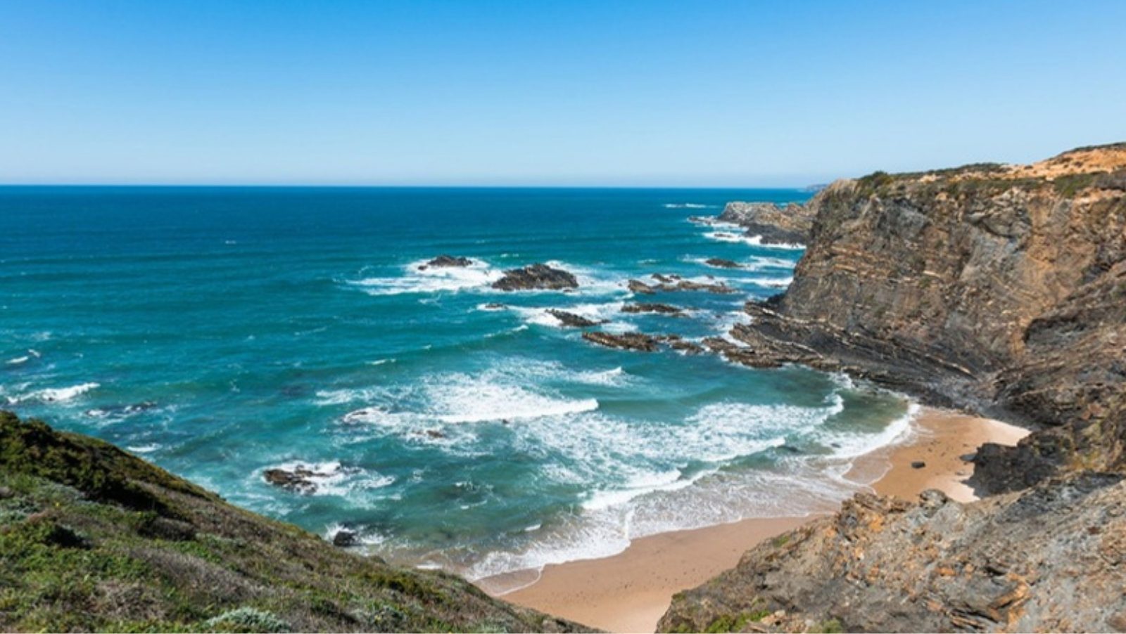 Rocky cliffs and a small sandy cove with turquoise Atlantic waves on the Alentejo coast in Portugal