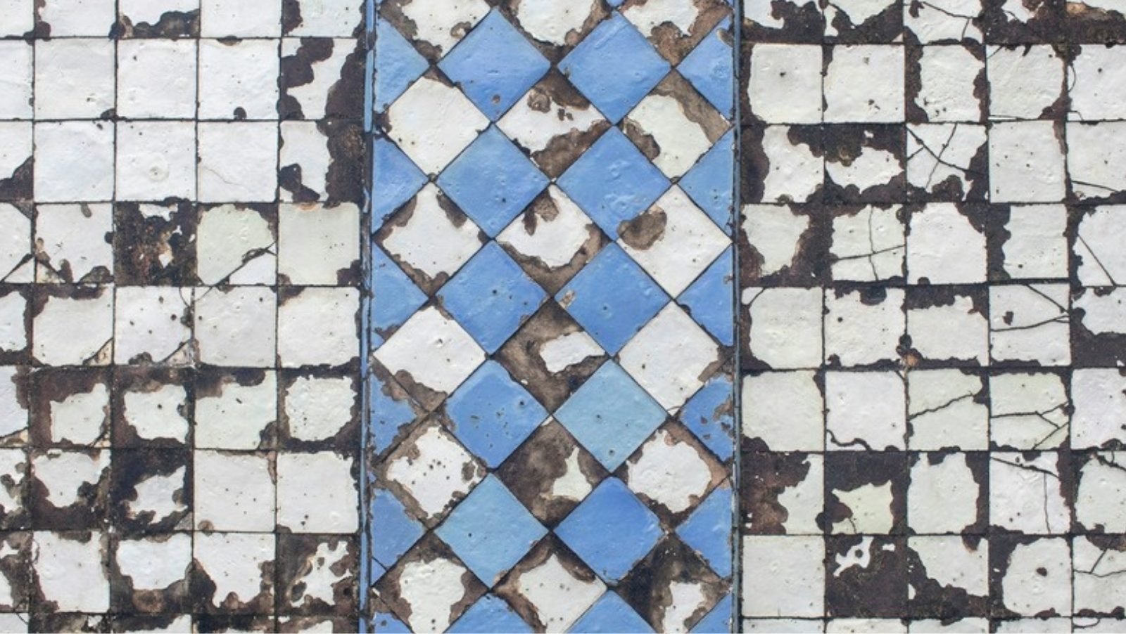 Weathered blue and white azulejo tiles with a diamond pattern on a wall in Portugal